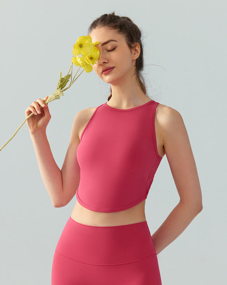Woman in brick red high-neck crop top and leggings holding a yellow flower to her face.