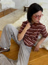 Model sits on floor wearing brown and white striped polo shirt with light gray jeans.
