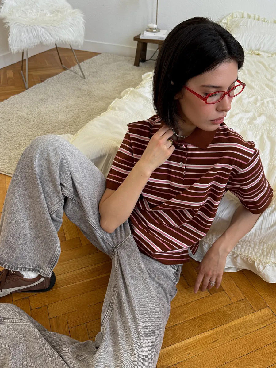 Model sits on floor wearing brown and white striped polo shirt with light gray jeans.