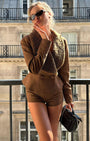 woman wearing brown suede jacket and shorts standing on a balcony