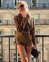 woman wearing brown suede jacket and shorts standing on a balcony