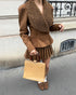 woman in brown suede jacket and pleated skirt holding beige handbag