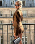 woman wearing brown suede jacket and shorts leaning on balcony railing
