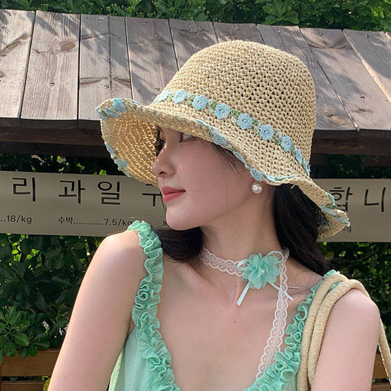 A woman wearing a beige straw hat with blue floral embroidery along the brim, pairing it with a matching pastel outfit for a summery look.