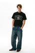 Model wearing a black chain graphic T-shirt with wide-leg blue jeans