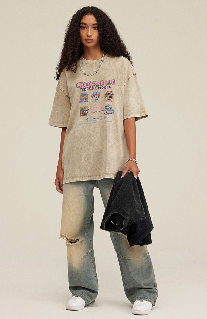 Woman in oversized khaki pixel tee holding black shirt and wearing loose jeans