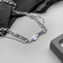 Close-up of silver necklace with blue engraved tag and layered links.