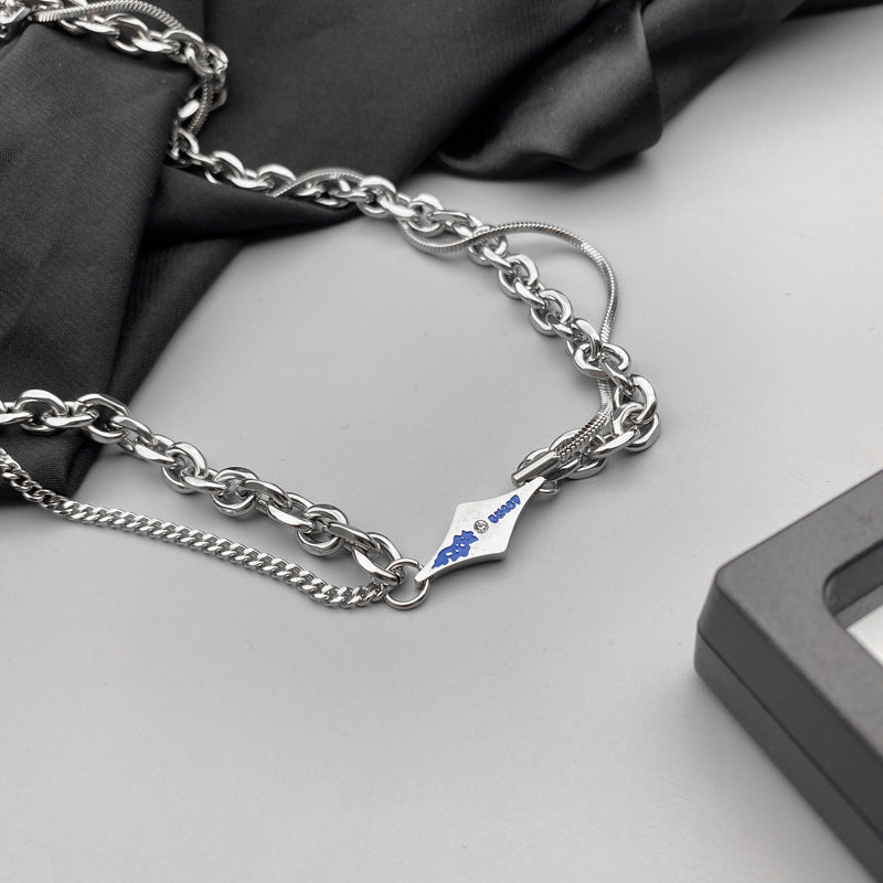 Close-up of silver necklace with blue engraved tag and layered links.