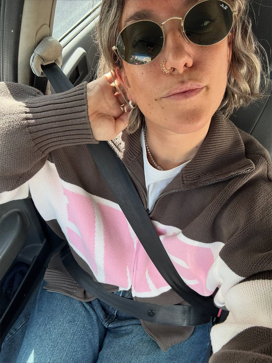 woman sitting wearing coffee brown jacquard letter zip up sweater with pink graphic