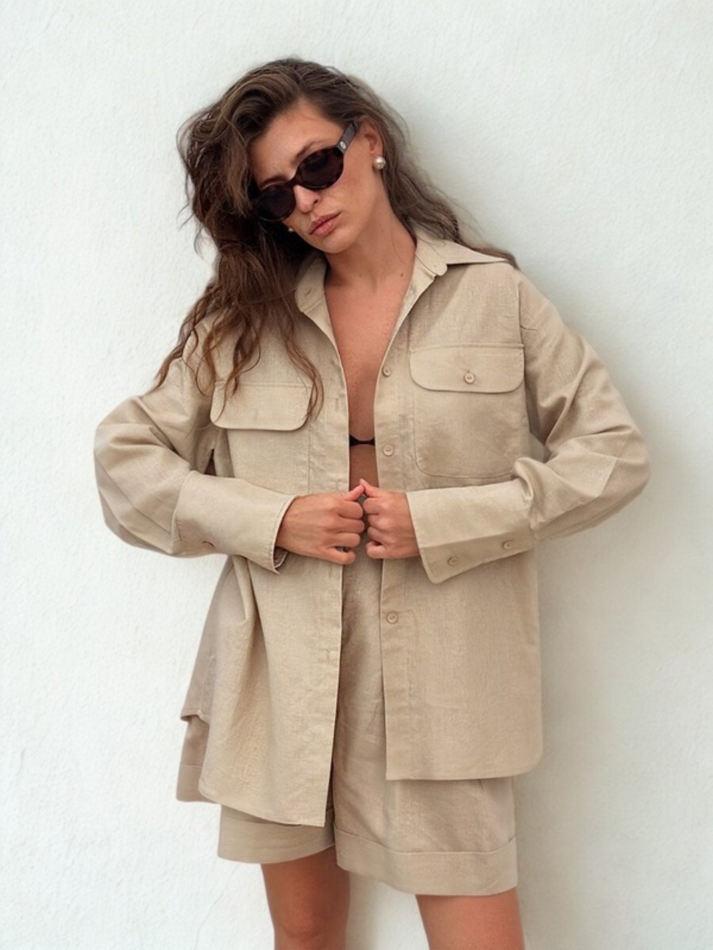 Woman in oversized khaki shirt and shorts posing in front of ocean view.