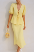 Woman wearing a yellow skirt set holding a mesh bag against a beige background