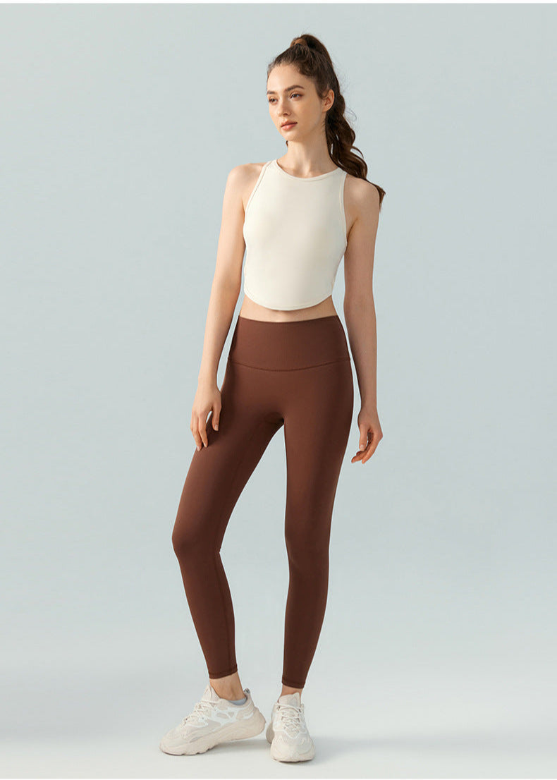 Full-body view of woman in ivory crop top and brown leggings, arms relaxed at sides.