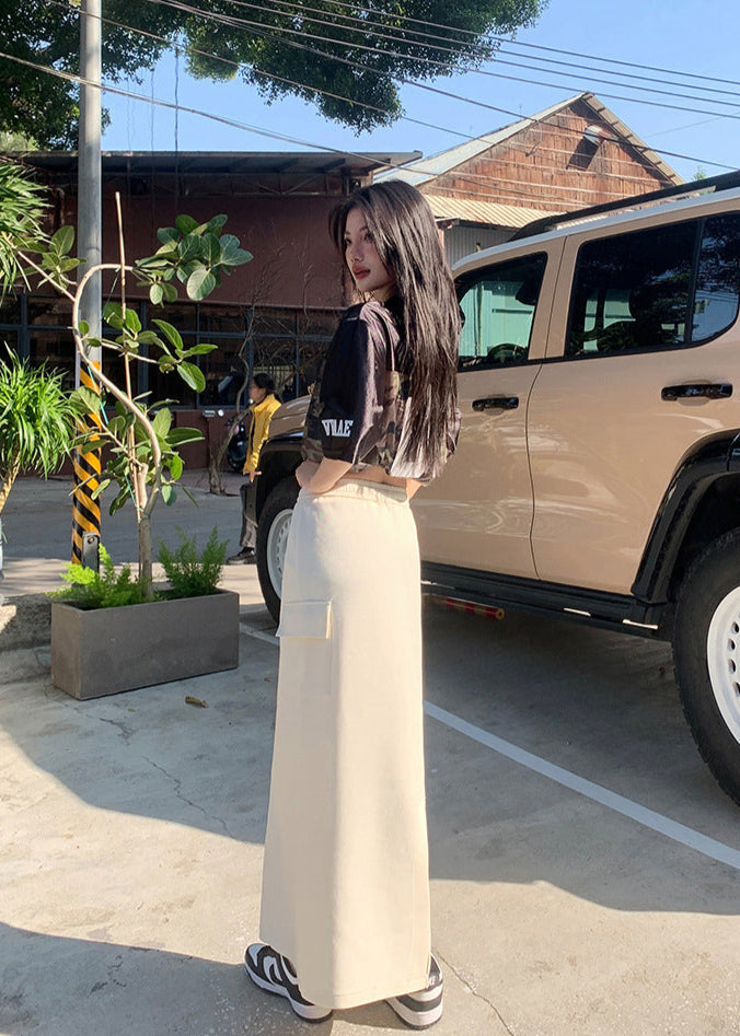 Model poses in sunlight wearing cream maxi skirt with side pocket and cropped camo top.
