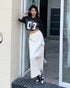 Model leans on doorway wearing cream maxi skirt with drawstring waist and cropped black top.