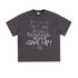 Flat-lay of dark purple oversized T-shirt with chalk-style text reading "There is but one secret to success: never give up!"