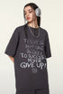 Close-up of model in dark purple oversized T-shirt with motivational quote on front, accessorized with headphones and necklace.