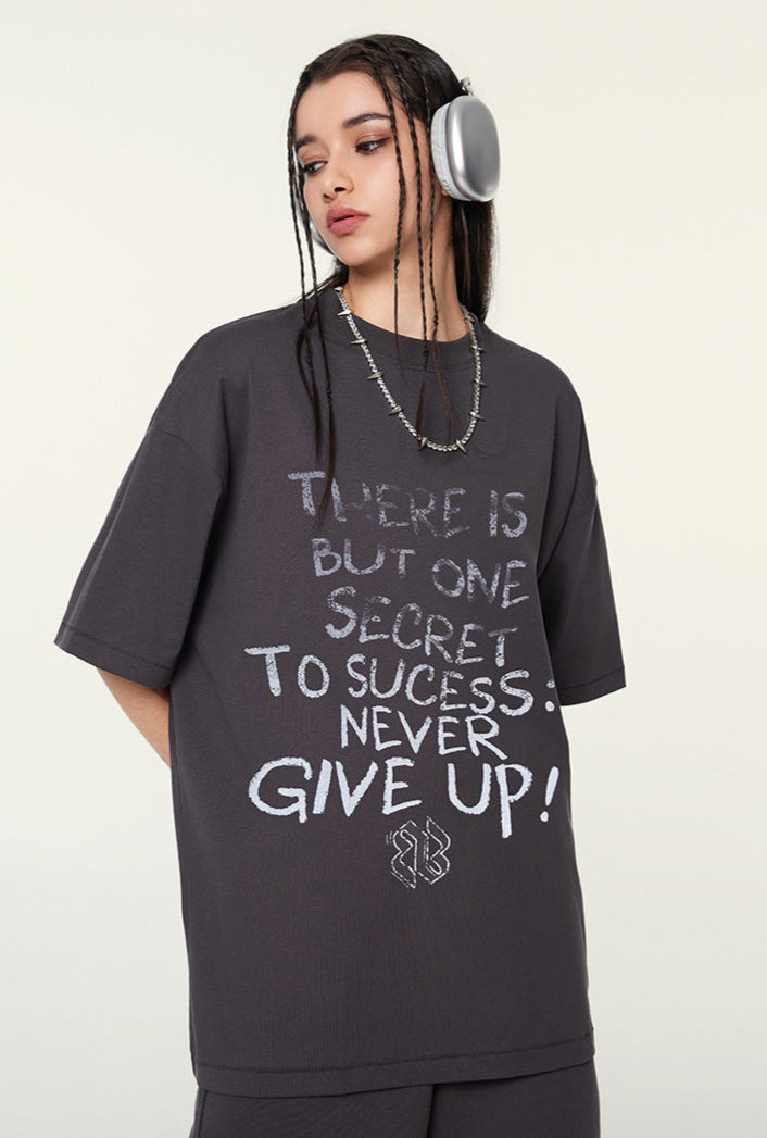 Close-up of model in dark purple oversized T-shirt with motivational quote on front, accessorized with headphones and necklace.
