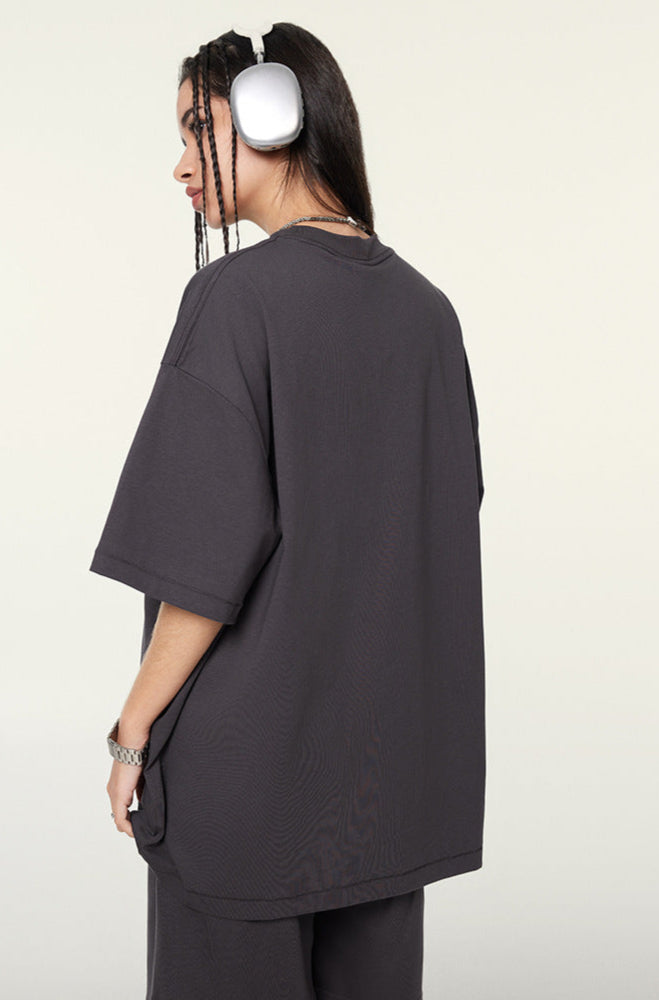 Side view of female model in dark purple oversized T-shirt and shorts, turning to reveal back.