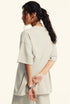 Woman poses with hands behind back wearing oversized offwhite  T-shirt.
