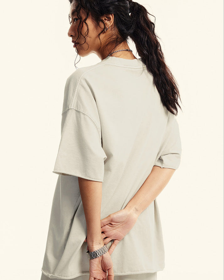 Woman poses with hands behind back wearing oversized offwhite  T-shirt.