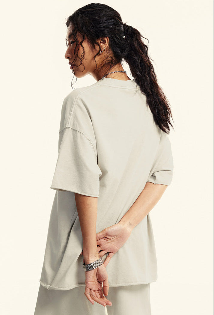 Woman poses with hands behind back wearing oversized offwhite  T-shirt.