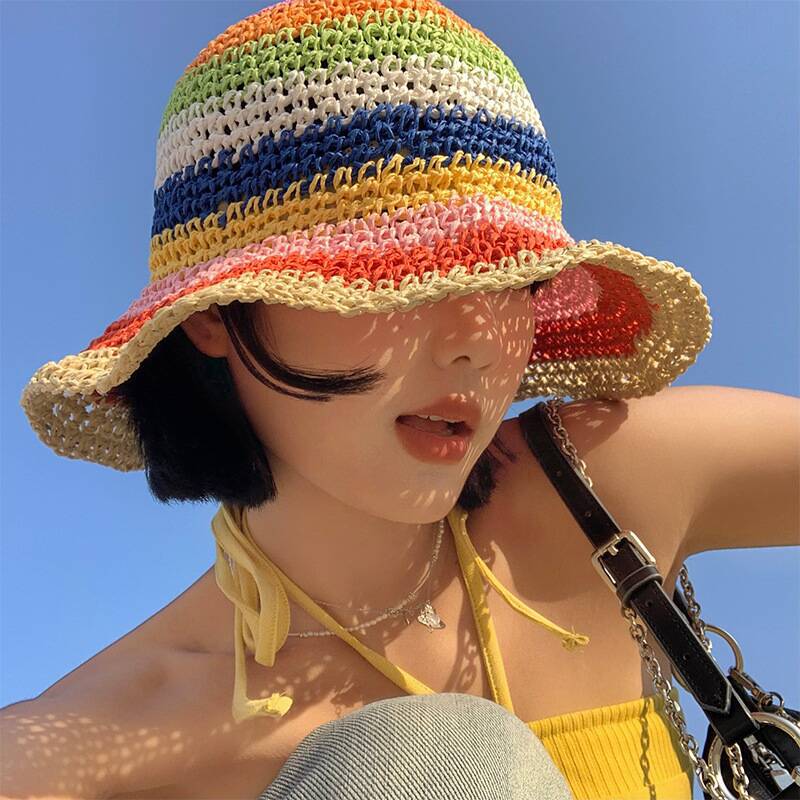 A woman wearing a colorful crochet bucket hat with rainbow stripes, paired with a yellow halter top under the bright blue sky.