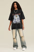 Model facing forward wearing black angel graphic tee and distressed jeans, arms relaxed at sides.