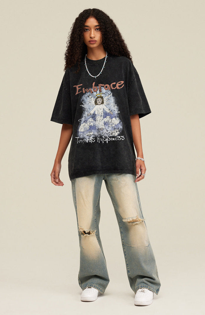 Model facing forward wearing black angel graphic tee and distressed jeans, arms relaxed at sides.