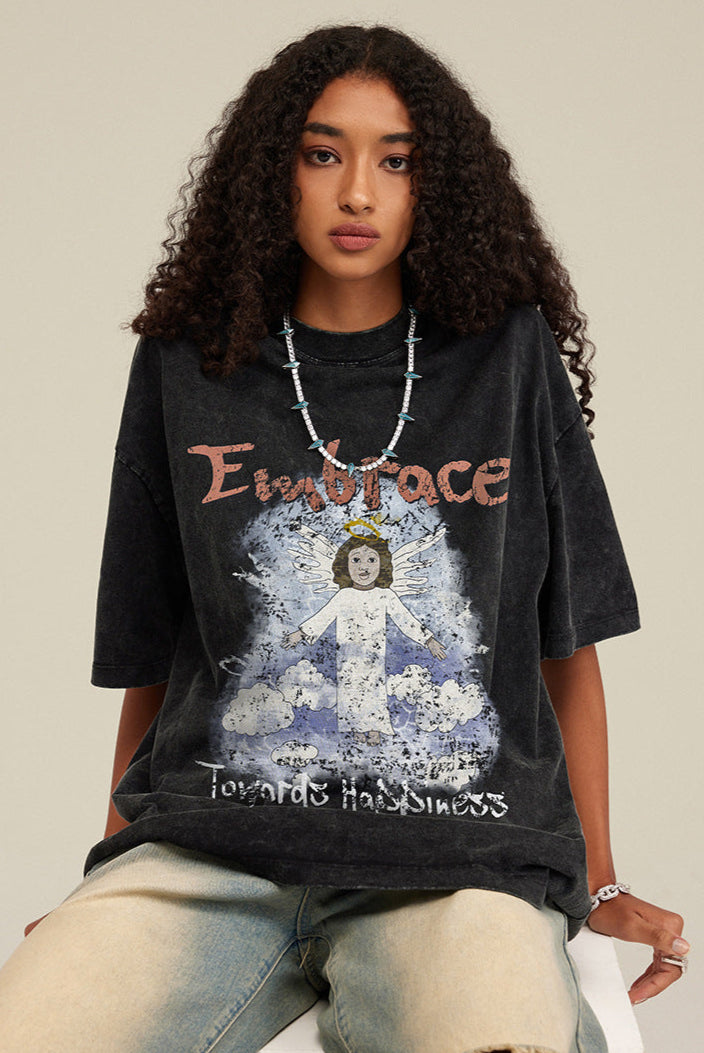 Model sitting while wearing black angel T-shirt, showing full print and necklace.