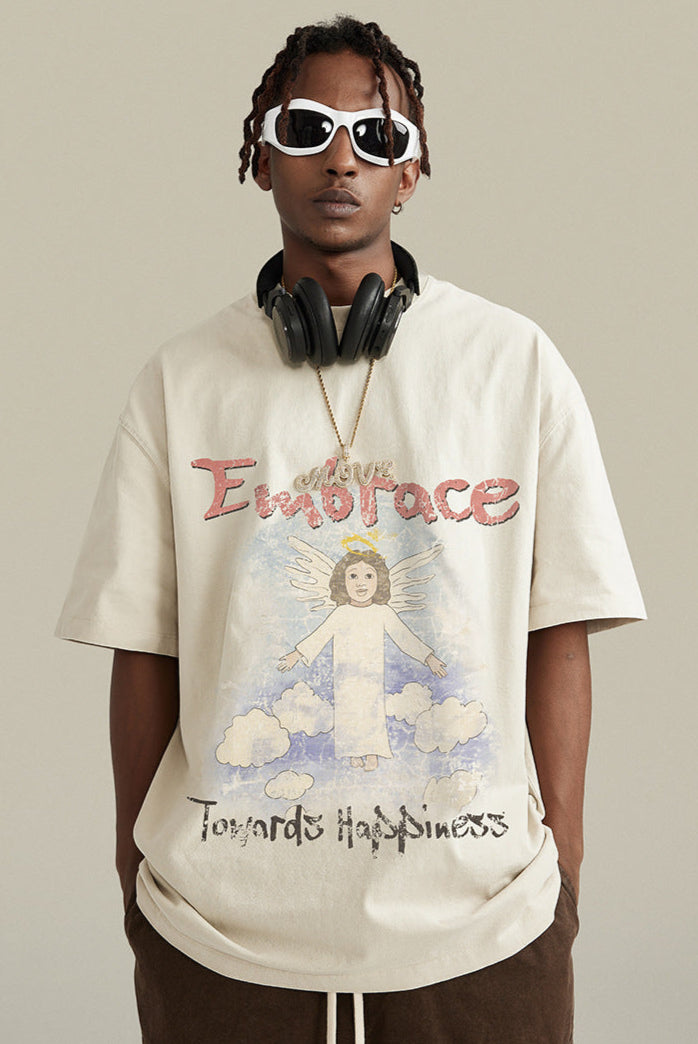 Model wearing cream angel graphic tee with headphones and brown cargo pants, standing pose.