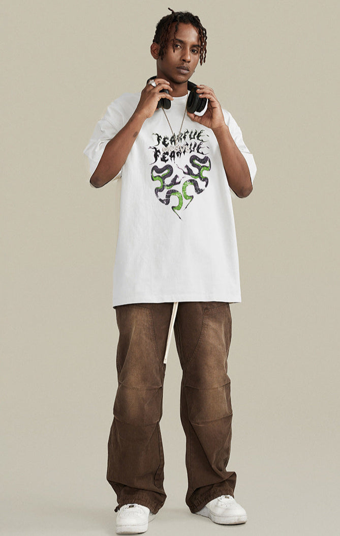 Model stands in white "Terrible Beauty" tee with green snake heart graphic.