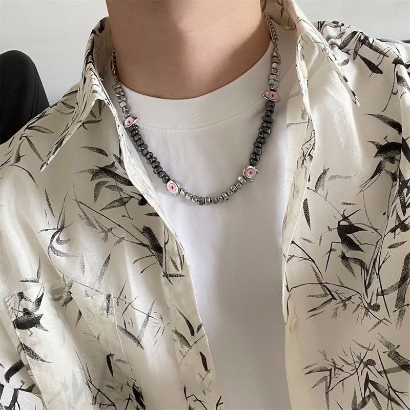 Man wears black and silver evil eye necklace with beaded texture.