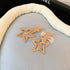 Gold-tone hollow star hair clips with a sleek metallic finish, displayed on a cushioned blue fabric.