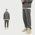 Man with short red hair wearing charcoal grey hoodie tracksuit with beaded necklace. Close-up shows relaxed joggers with beige Air Jordan 4 sneakers