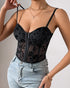 Woman adjusting strap of sheer black floral corset bustier styled with denim jeans.