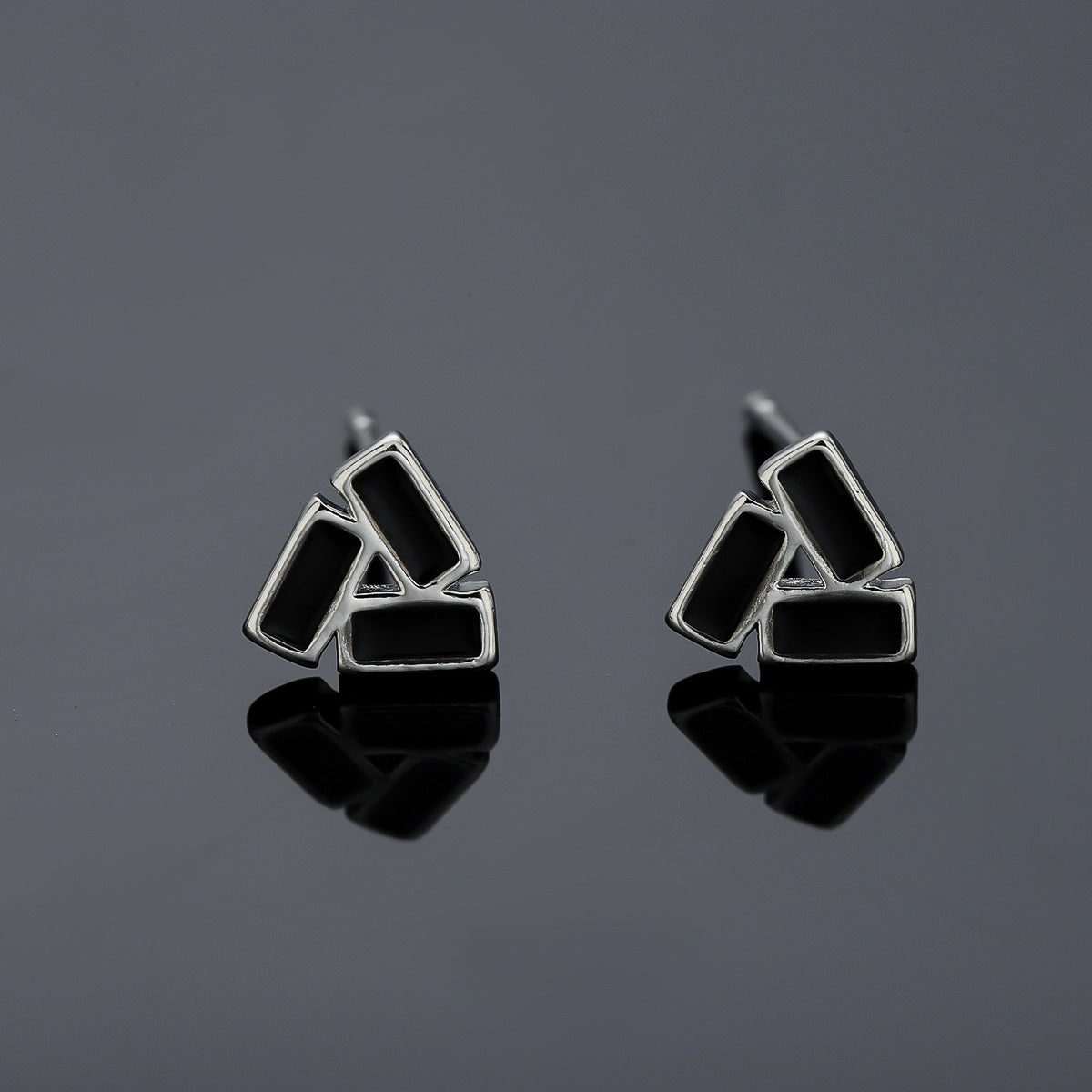 Pair of geometric black and silver colored stud earrings on glossy surface.