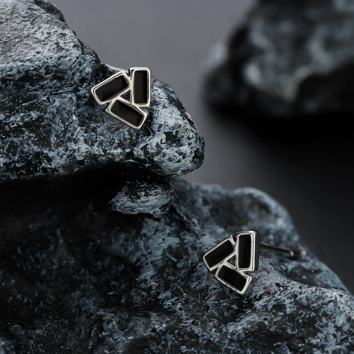 Geometric black stud earrings set on dark stone surface.
