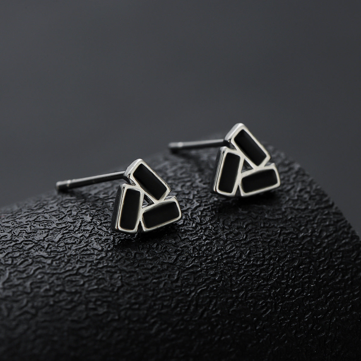 Geometric stud earrings displayed on textured black cylinder.