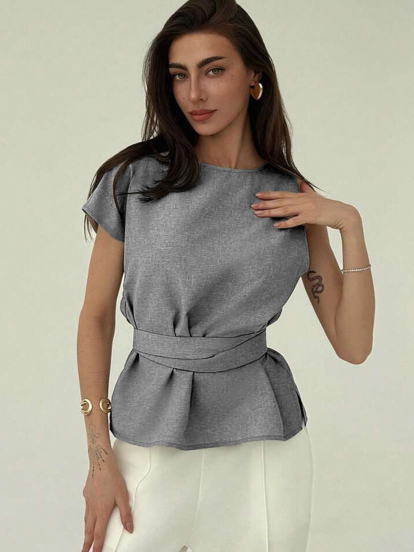 Gray sleeveless belted top styled with white pants, front view