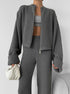 Person wearing a gray knit lounge setwith a cropped jacket and pants on a plain background