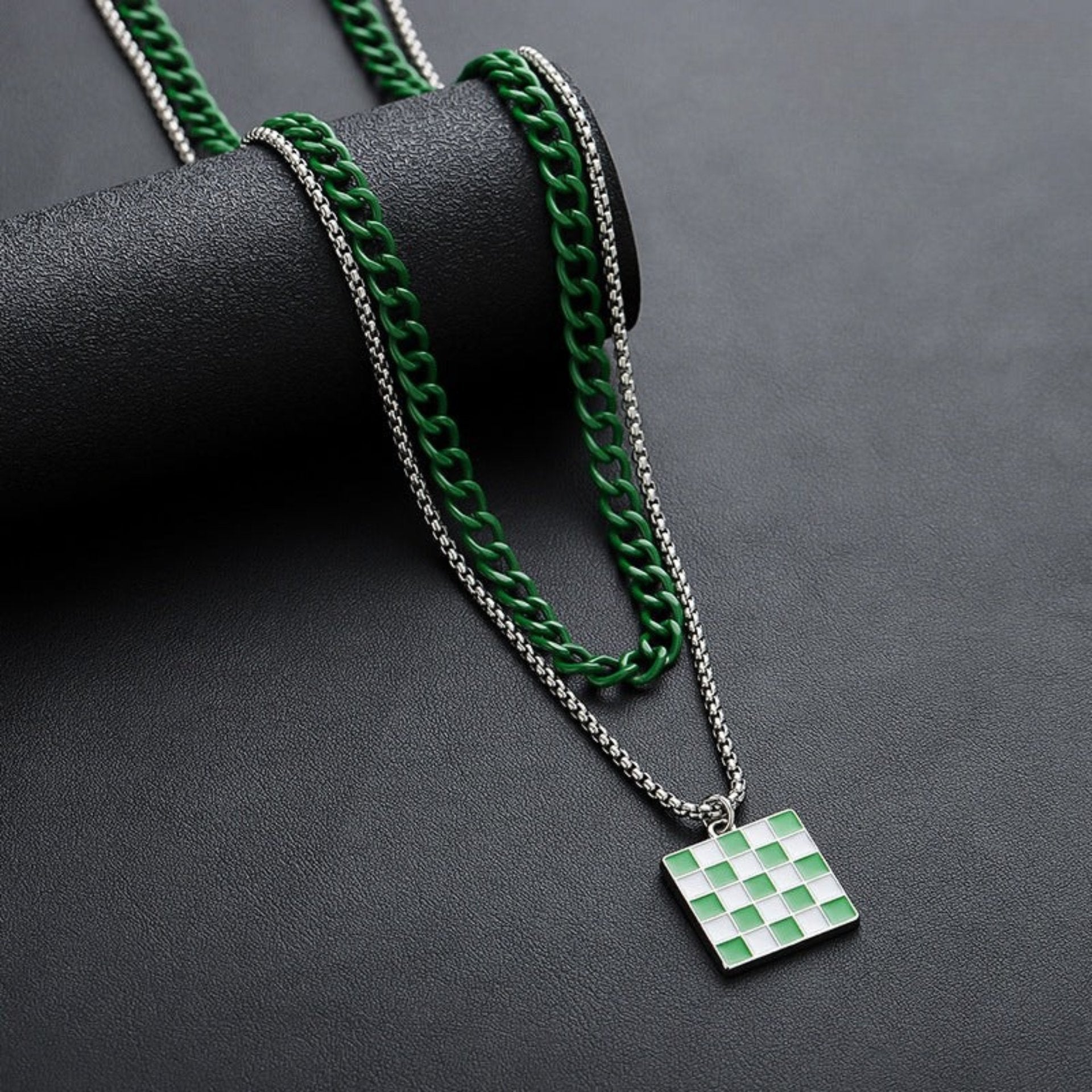 Green and silver layered chain necklace with square checkerboard pendant on display roll.