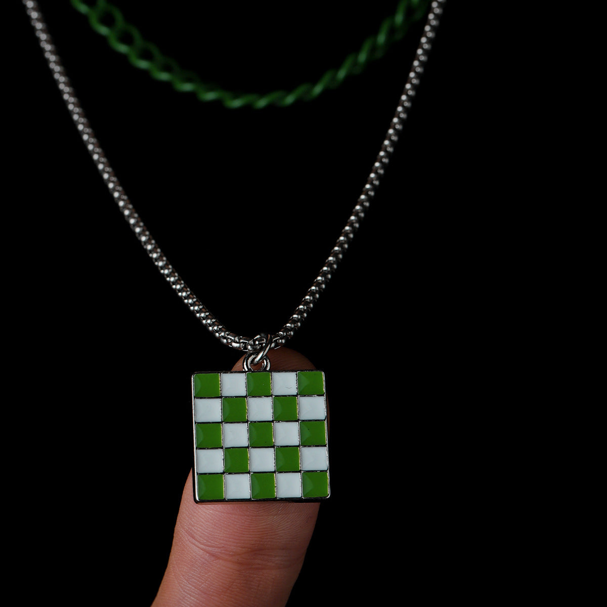 Finger holding square checkerboard pendant hanging from double chain.