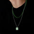 Green checkerboard pendant necklace worn over black shirt.