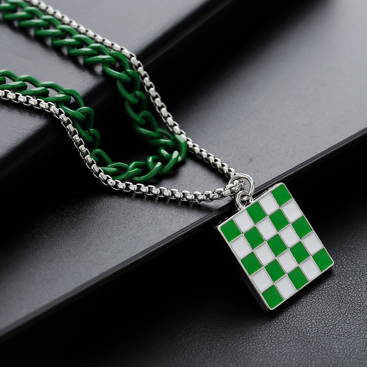 Close-up of green and silver chains with enamel checkerboard pendant.