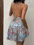 Back view of woman wearing a floral backless sundress against a plain wall
