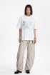Full body view of a model wearing a white relaxed graphic t-shirt with beige wide-leg trousers.