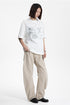 Model posed in a white short sleeve graphic crewneck t-shirt and wide-leg casual pants.