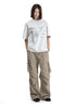 Full body shot of a model wearing a heather grey graphic tee with tan cargo pants and black shoes.
