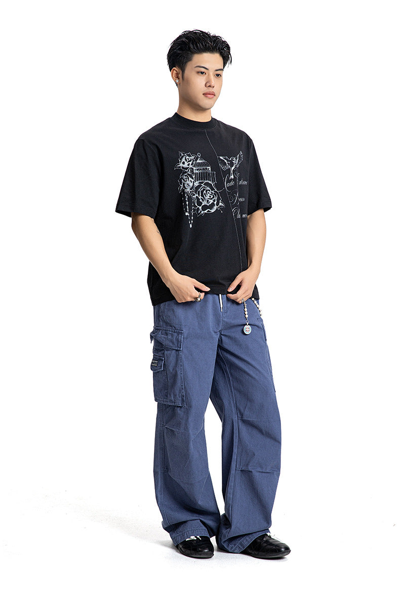 Full body shot of a male model wearing a black loose fit graphic crewneck tee with blue cargo pants.