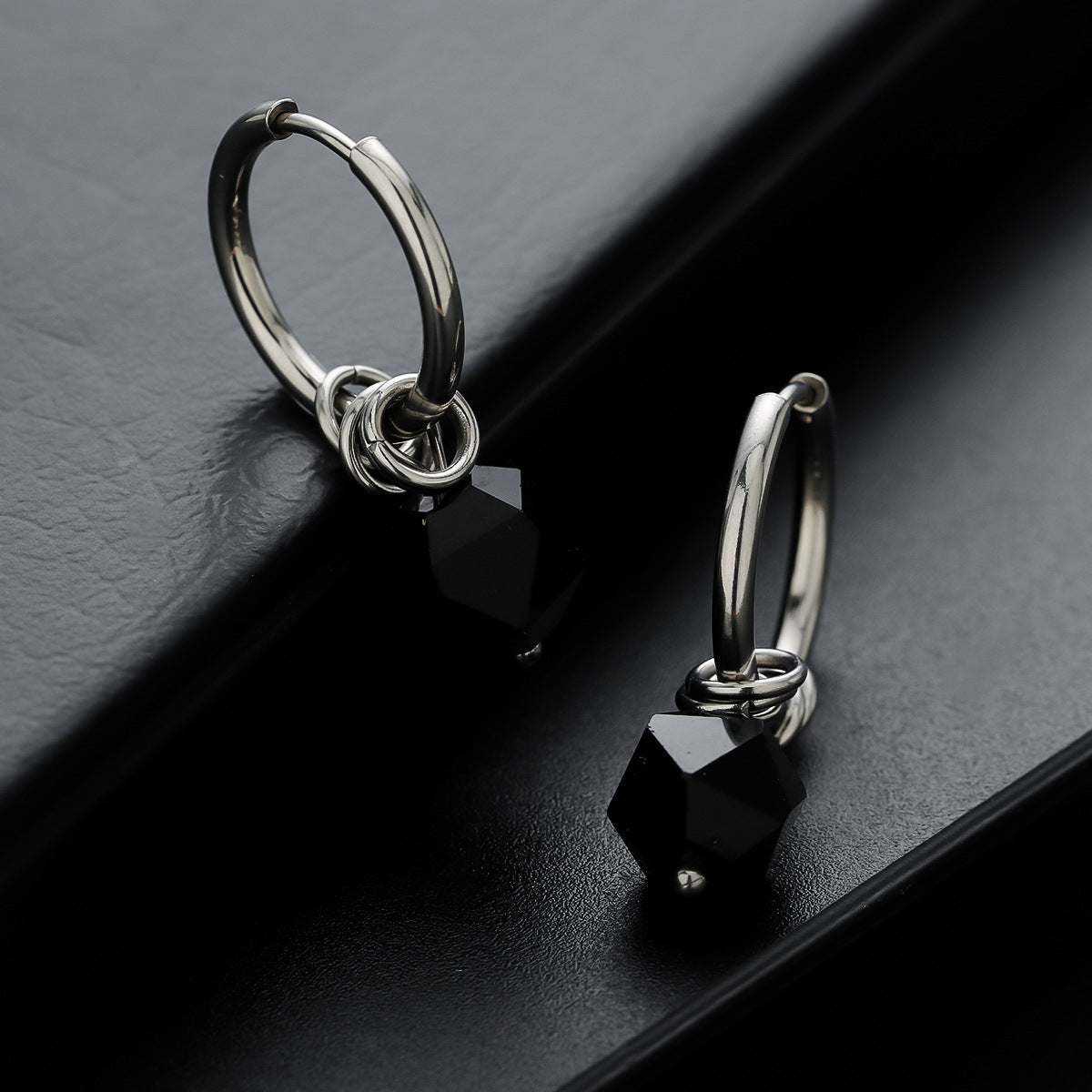 Silver hoop earrings with black hexagon zircon drops on dark background.
